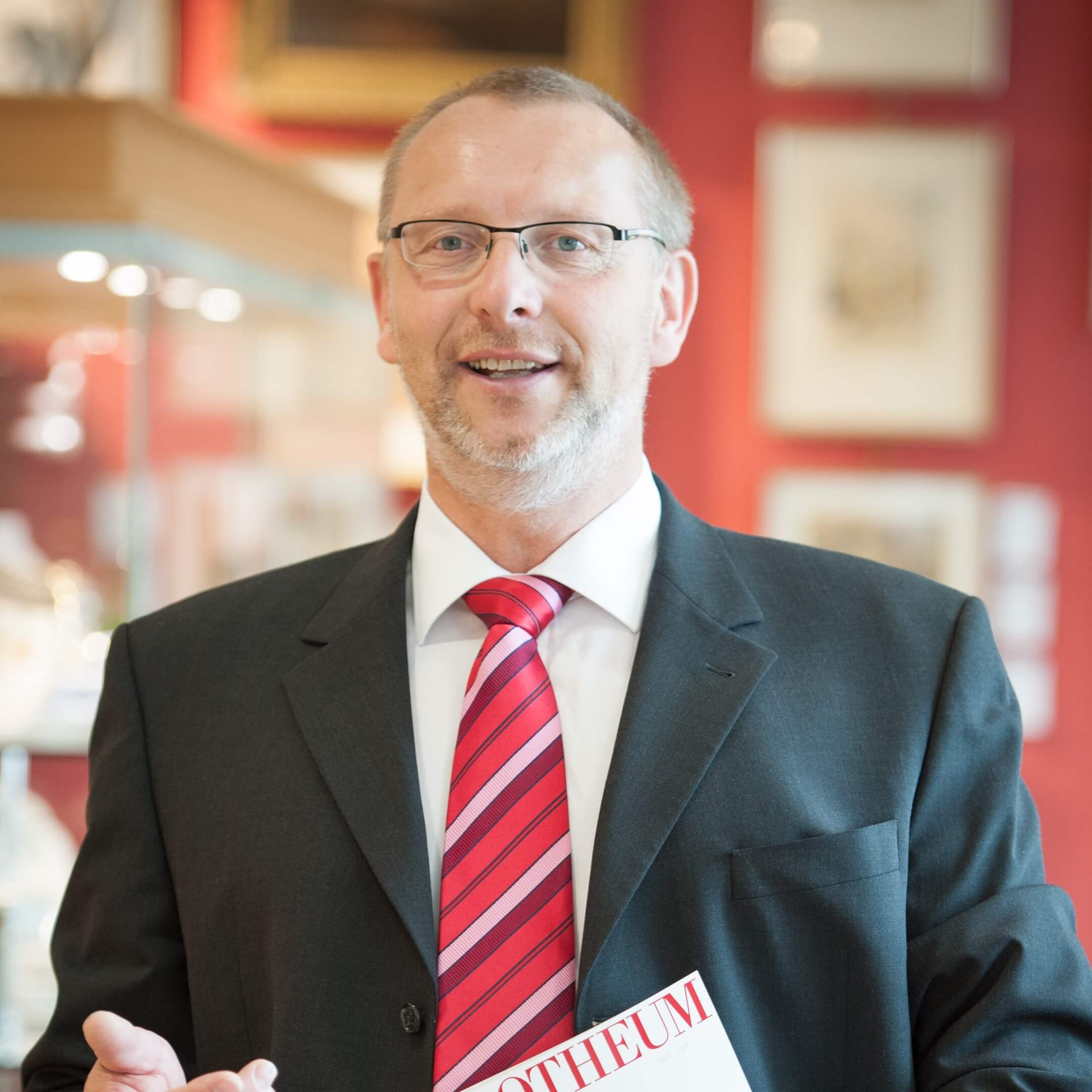 filialleiter-in-anzug-in-der-filiale-vor-bildern-und-einer-vitrine