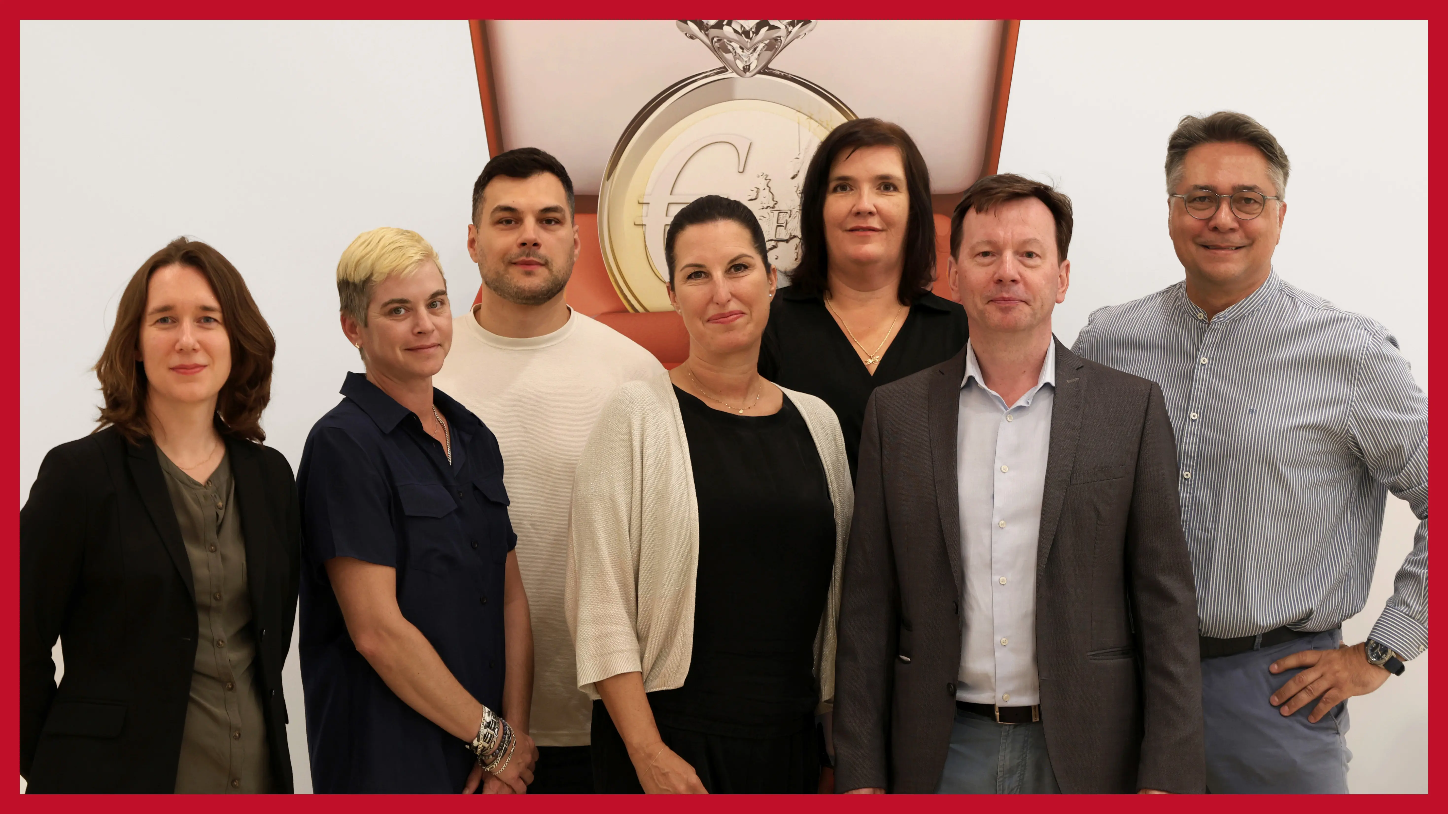 sieben-koepfiges-team-steht-vor-poster-eines-wertgegenstandes