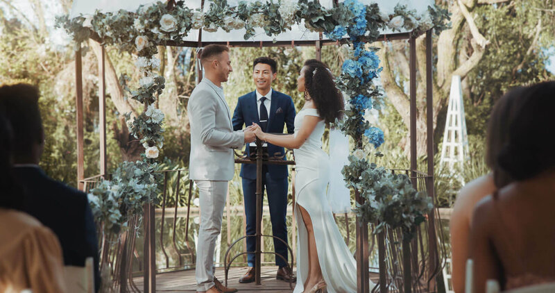 Hochzeitsbudget: Das Bild zeigt eine Frau und einen Mann in Hochzeitskleidung, dieunter einem blumengeschmückten Traubogen stehen und  sich in der Natur das Ja Wort geben